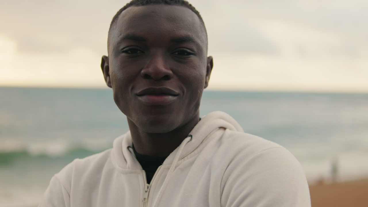 Happy Young Black Man in Hoodie Smiling by the Sea