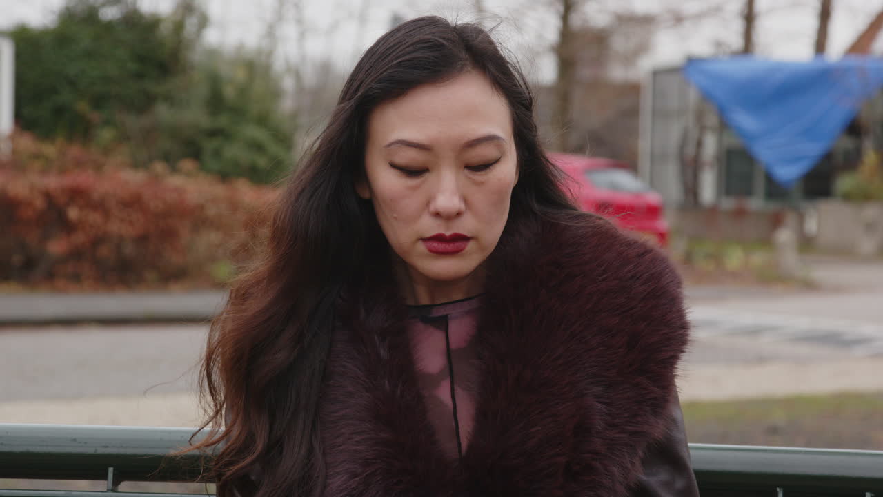 Close-up de uma mulher asiática emocionada sentada em um banco em um parque no outono