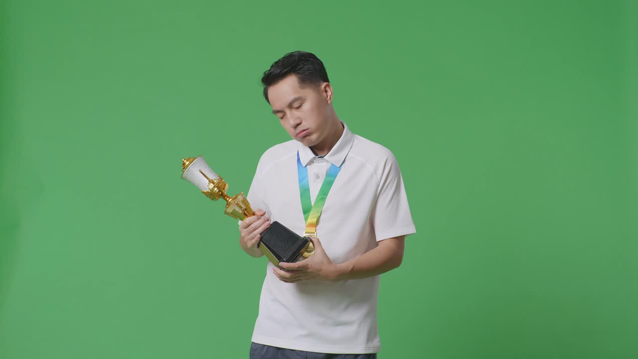 금메달을  아시아인이 트로피를 쳐다보며 머리를 흔들며 불만을 표하며 스튜디오의 녹색 스크린 배경에서 첫 번째 우승자로 승리합니다.