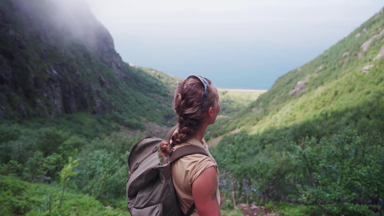 mujer excursionista en mochila de pie en una exuberante montaña verde disfruta de vistas a la montaña donnamannen, nordland, noruega