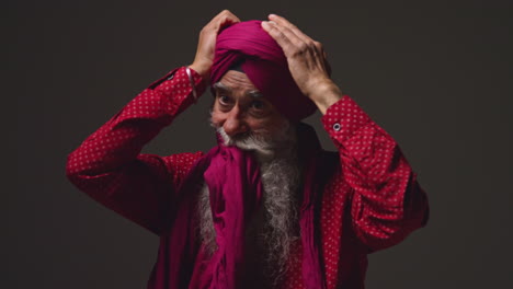 fotografía de iluminación de estudio de baja clave de un hombre sikh anciano con barba atando tela para turbante contra un fondo oscuro 12