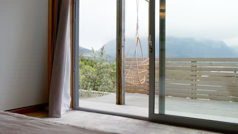 open sliding door revealing cozy balcony with hanging chair and scenic mountain view, copy space