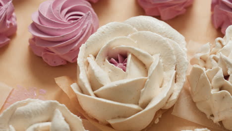 close up of beautifully crafted flower-shaped white dessert with pink center surrounded by neatly arranged pink swirl cupcakes on parchment paper in warm kitchen lighting