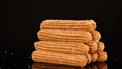 golden churros are stacked in a geometric arrangement, rotating smoothly against a glossy black backdrop with dramatic studio lighting and crisp focus
