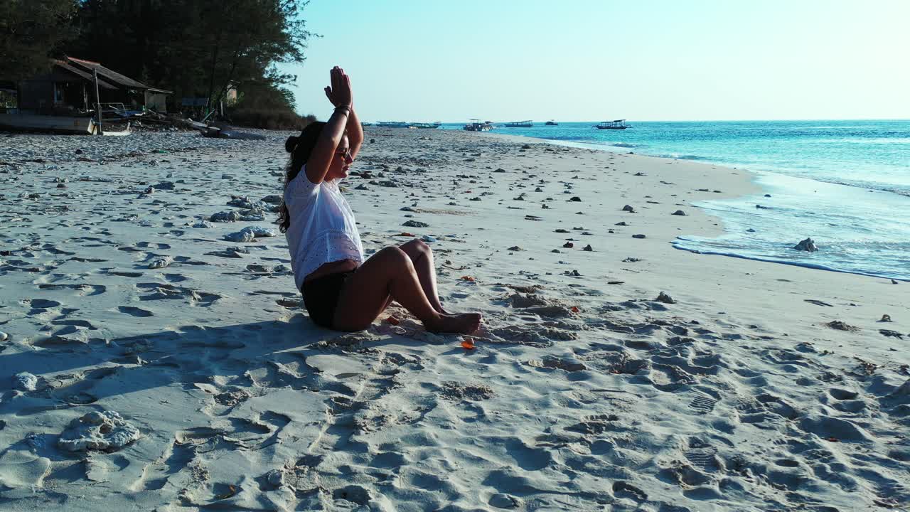 Mujer joven haciendo yoga en la arena blanca de una playa exótica frente al mar en calma al amanecer, Filipinas.