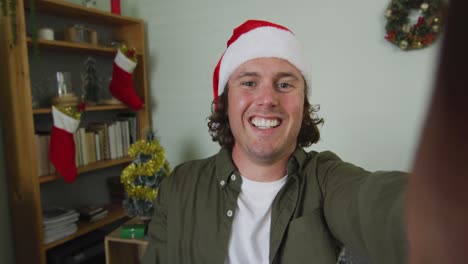 happy caucasian man in santa hat on christmas video call waving and talking