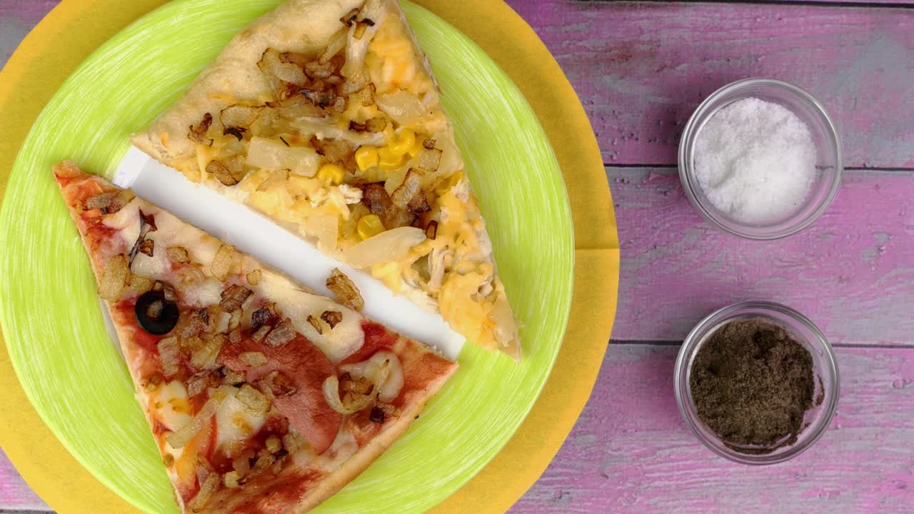 dos pedazos de pizza con tomates, salchichas, mozzarella y aceitunas en el plato gira lentamente sobre un fondo rosado.
