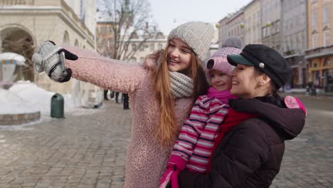 sisters tourists taking selfie, posing, making video conferencing on mobile phone on city street