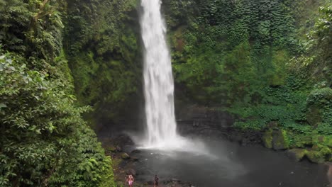 a drone pulls back to reveal swimmers at the base of nungnung falls in bali, indonesia