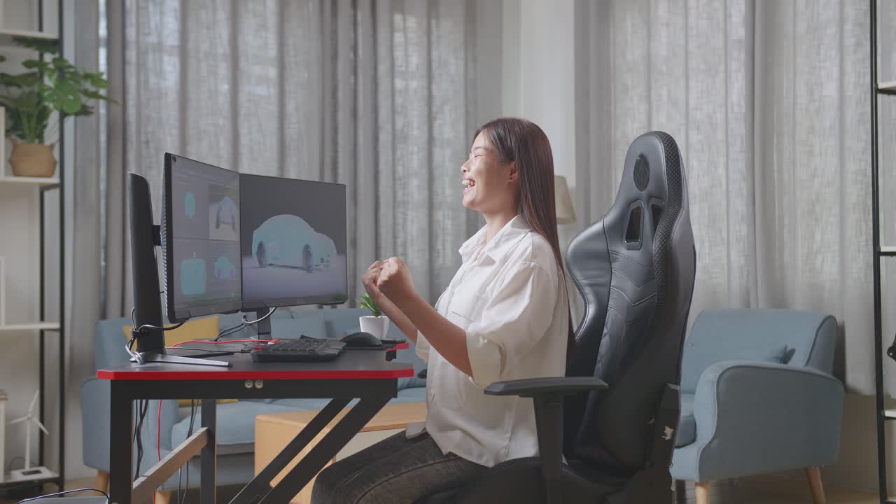 아시아 여성 자동차 디자이너의 측면 뷰는 목표를 외치며, 스튜디오에서 데스크 컴퓨터에서 ev 자동차의 3d 모델을 작업하는 동안 성공 축하를 위해 춤을 추고 있습니다.