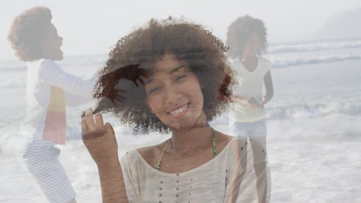 Sulla spiaggia, donna con capelli ricci che sorride, con animazione di amici che giocano sullo sfondo