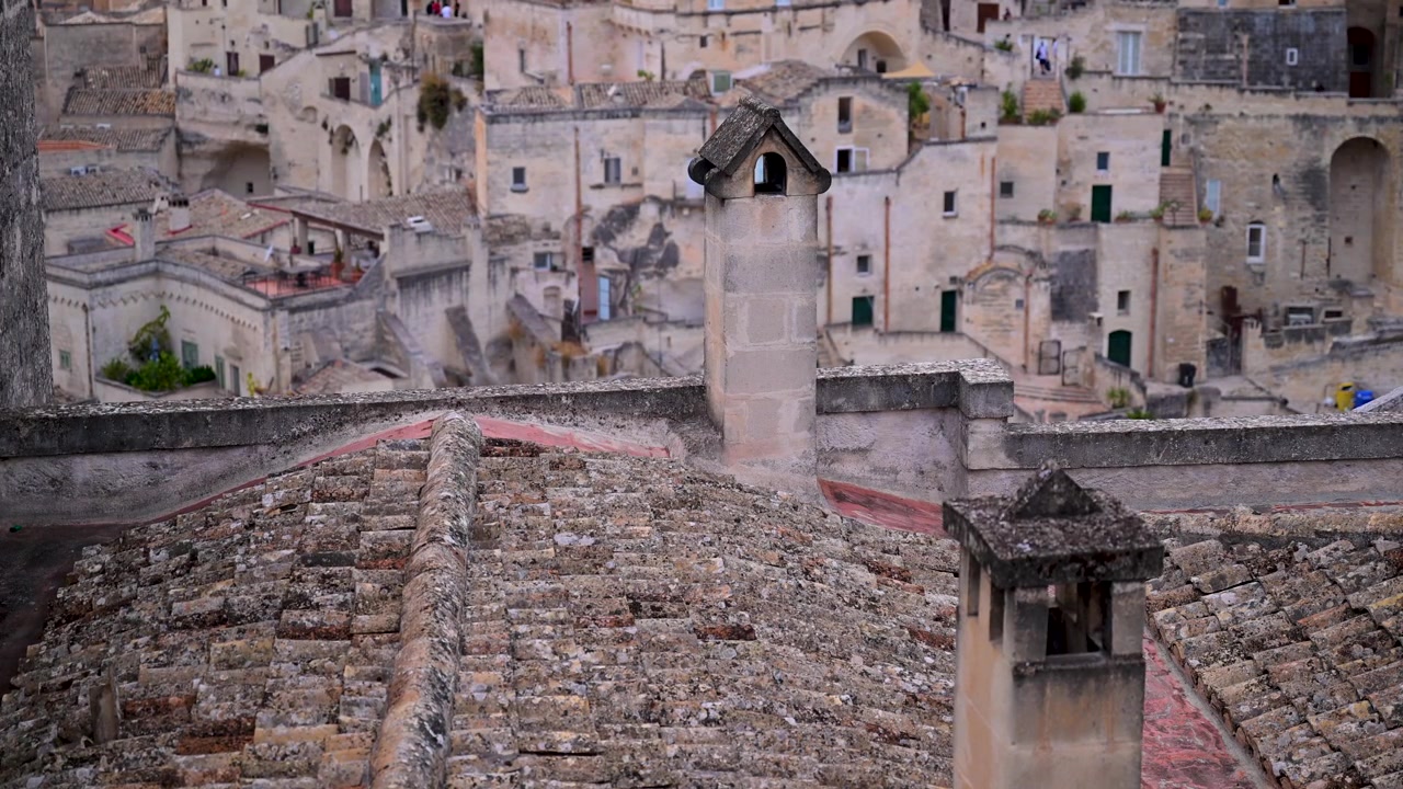 Vecchi tetti in tegole e camini in pietra si ergono di fronte ad abitazioni rupestri densamente raggruppate nel quartiere storico dei Sassi di Matera