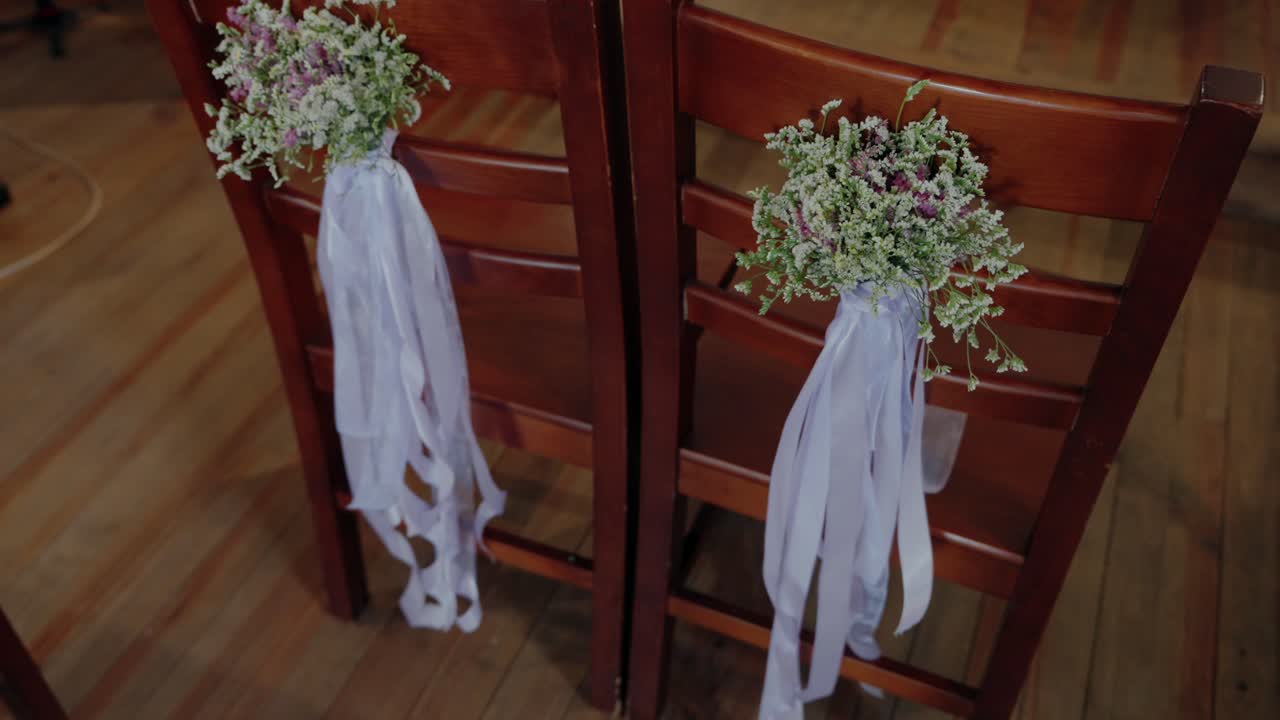 Deux chaises en bois décorées de petits bouquets floraux et de longs rubans blancs pour un événement de mariage.