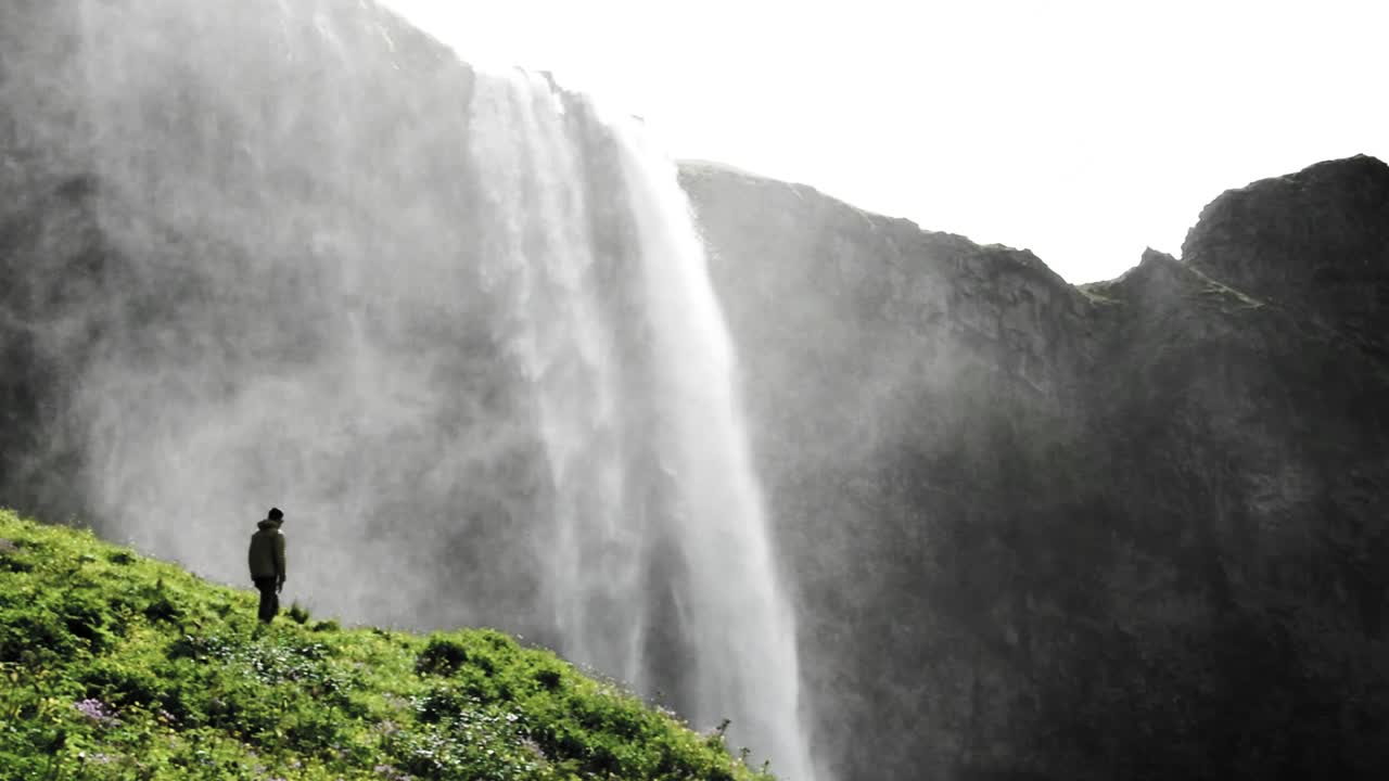vista impresionante de la cascada seljalandsfoss en islandia con un hombre caminando hacia ella para verla más de cerca