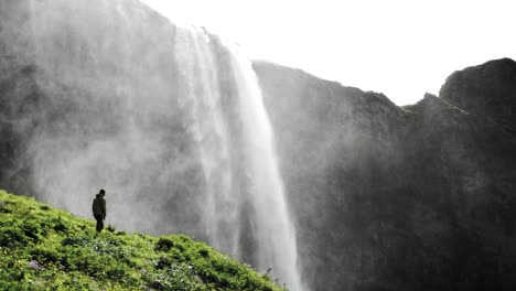 Vista-Impresionante-De-La-Cascada-Seljalandsfoss-En-Islandia-Con-Un-Hombre-Caminando-Hacia-Ella-Para-Una-Vista-Más-Cercana