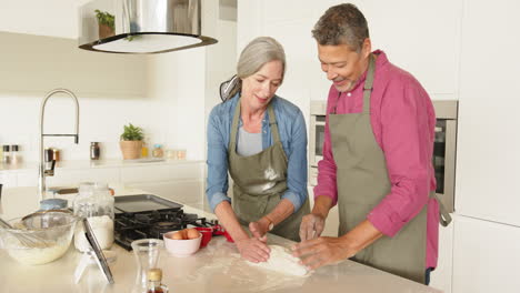 baking, multiracial senior couple preparing dough in modern kitchen, enjoying cooking time, at home