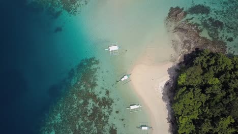 Vista-Aérea-De-Una-Playa-De-Arena-Blanca-En-Una-Isla-Tropical-Con-Barcos-Filipinos-Tradicionales-En-Aguas-Azules-Perfectas-En-Filipinas---Pedestal-De-Seguimiento-De-Cámara-Hacia-Abajo