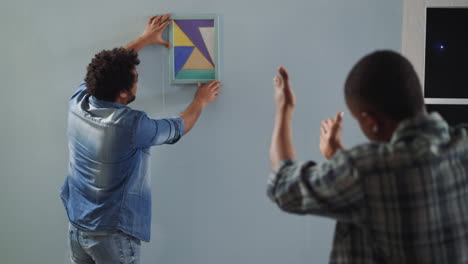 hombres afroamericanos cuelgan dibujos abstractos en la pared en el estudio