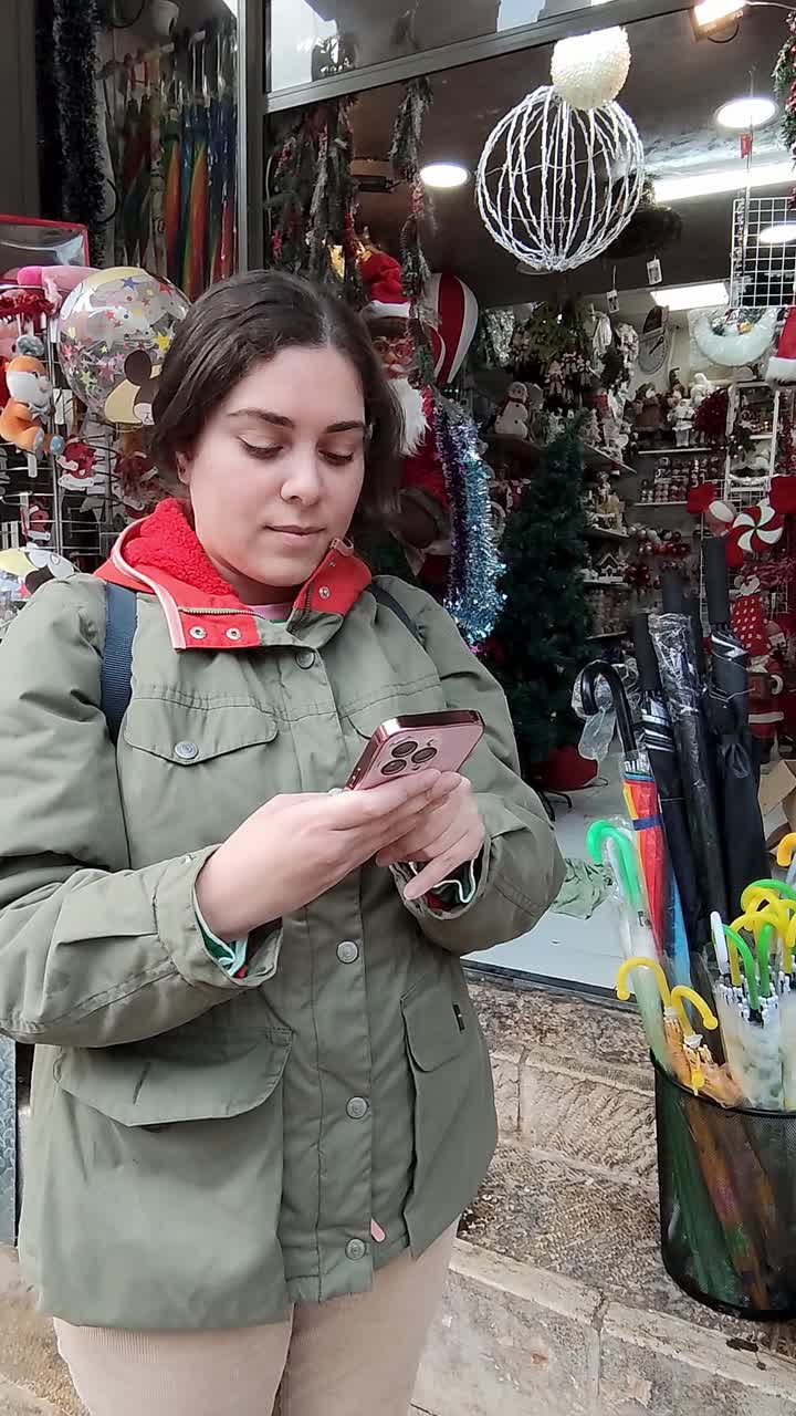 A woman is looking at her phone while standing in front of a Christmas tree
