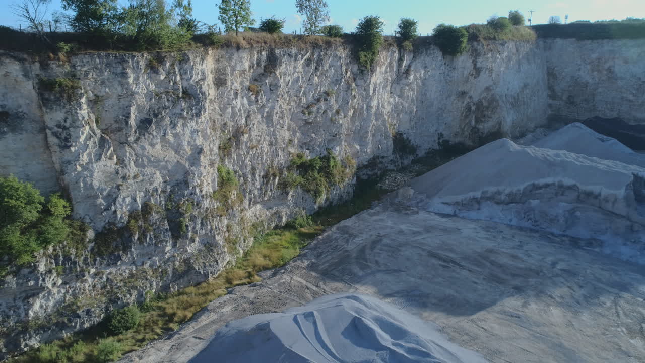toma de drones de una pequeña cantera de piedra caliza a cielo abierto con montones de grava y acantilados blancos con pequeños árboles en la parte superior en yorkshire, reino unido