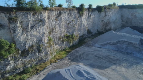 drone shot of small openpit limestone quarry with heaps of gravel and white cliffs with small trees on top in yorkshire uk