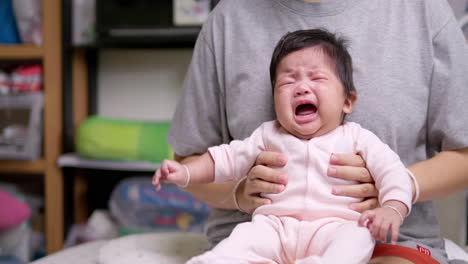 어머니의 무에 앉아 있는 신생아는 분홍색 옷을 입고 팔과 다리를 는 동안 눈물을 흘리고 있습니다.