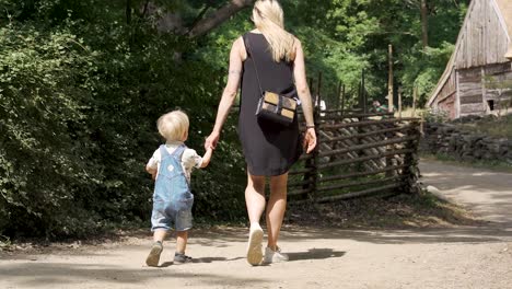 young caucasian mother and two years old boy holding hands walking down a trail in a rural village in old denmark during summer slow motion