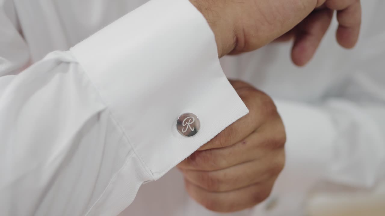 Close up of silver cufflink with engraved 'R' on white dress shirt during wedding prep