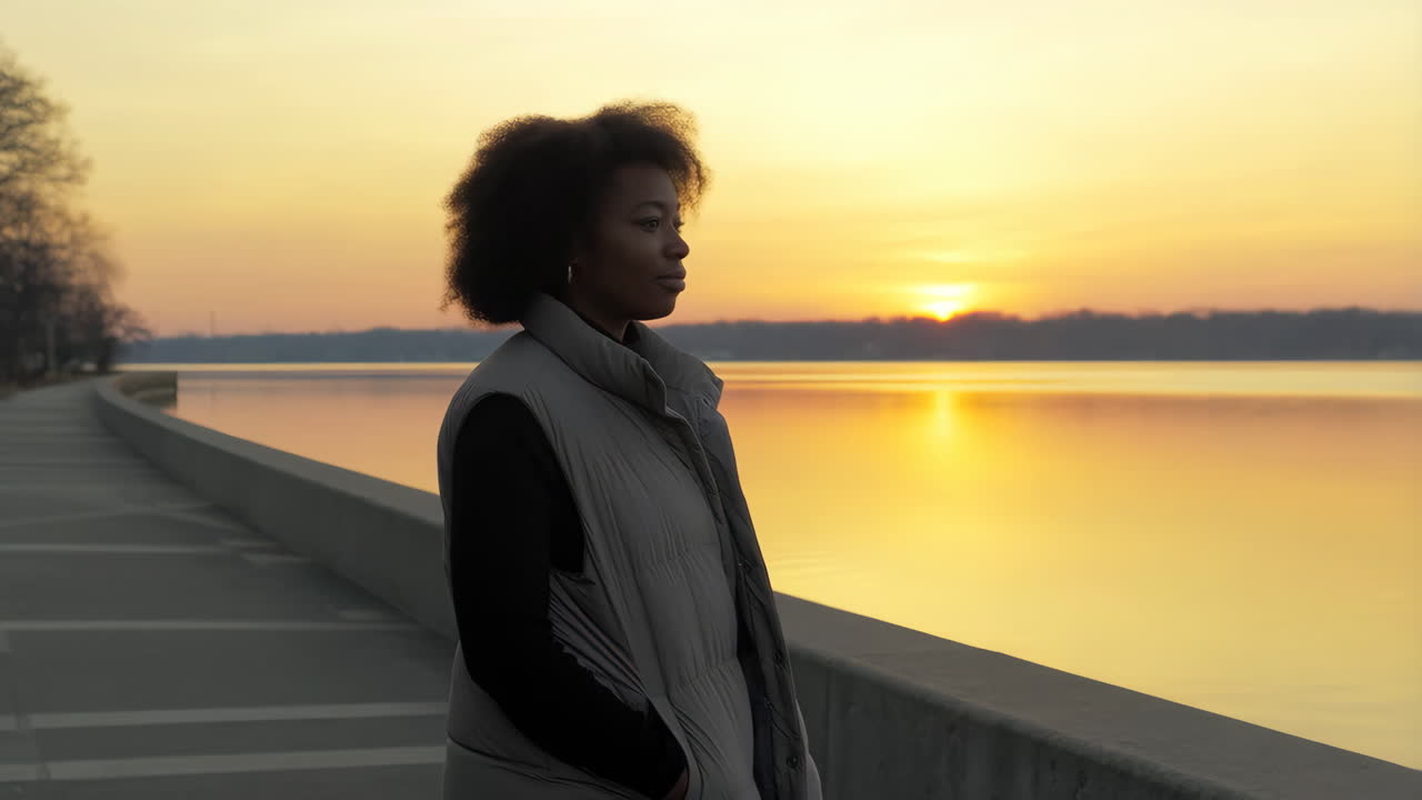 Junge afroamerikanische Frau steht am See bei goldenem Sonnenuntergang