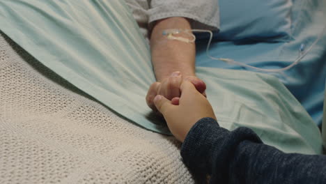 little boy holding grandmothers hand granny lying in hospital bed child showing affection at bedside for grandparent recovering from illness health care family support