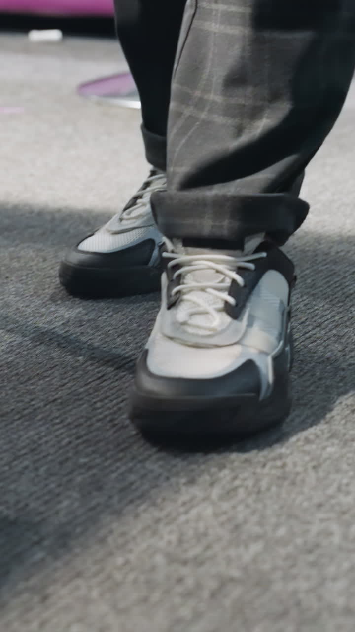 primer plano de una figura masculina con pantalones negros y zapatillas de deporte caminando por el suelo alfombrado. la sombra y el movimiento enfatizan el movimiento. calzado moderno y estilo casual visibles, con iluminación dinámica