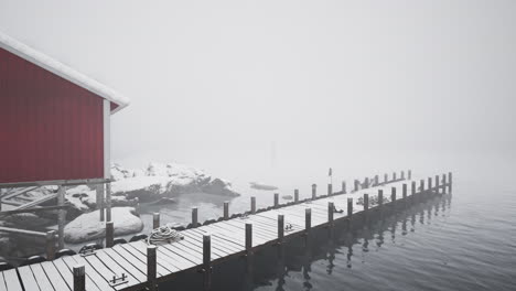 snowy pier and red house in foggy winter landscape
