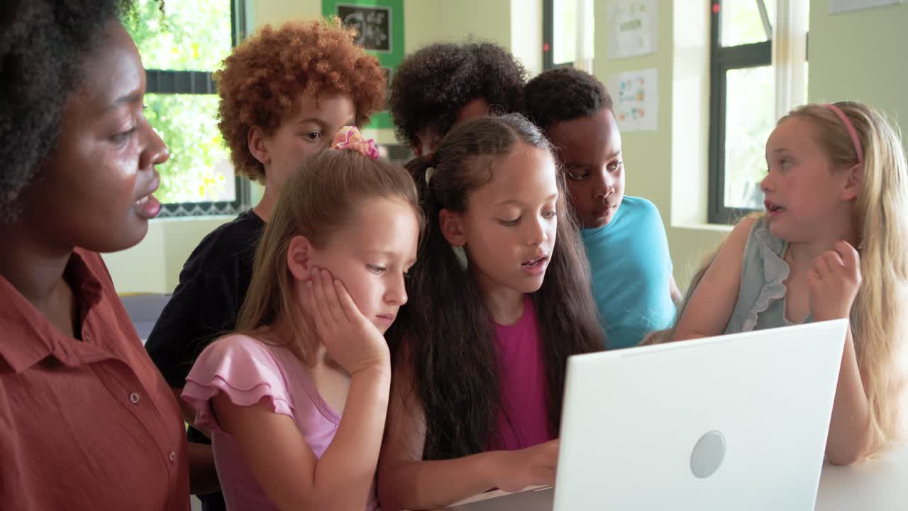 African American teacher in rust top guiding children using white laptop in classroom to learn