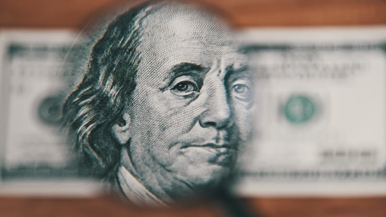 Cento dollari visti sotto una lente d'ingrandimento su un tavolo di legno