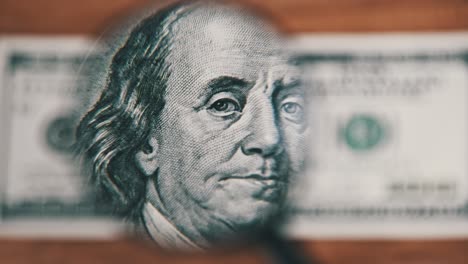 one hundred dollars look under magnifying glass on wooden table