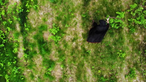 Vista-Aérea-De-Un-Espeluznante-ángel-De-La-Muerte-Con-Guadaña-Caminando-En-Un-Bosque-Verde