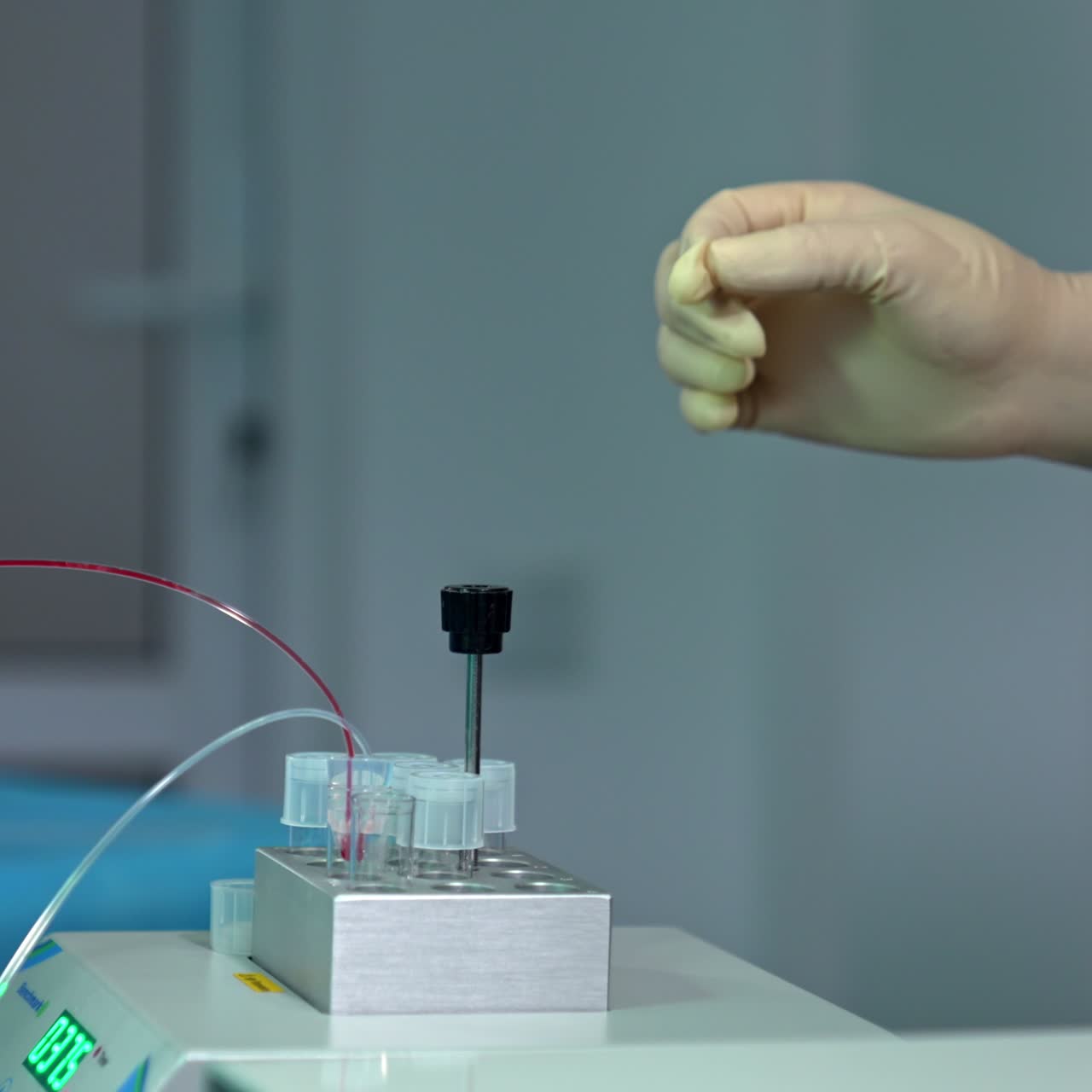Liquids filling the test tubes. Medic's hand in gloves waiting the reservoirs to fill. Close up. Blurred backdrop