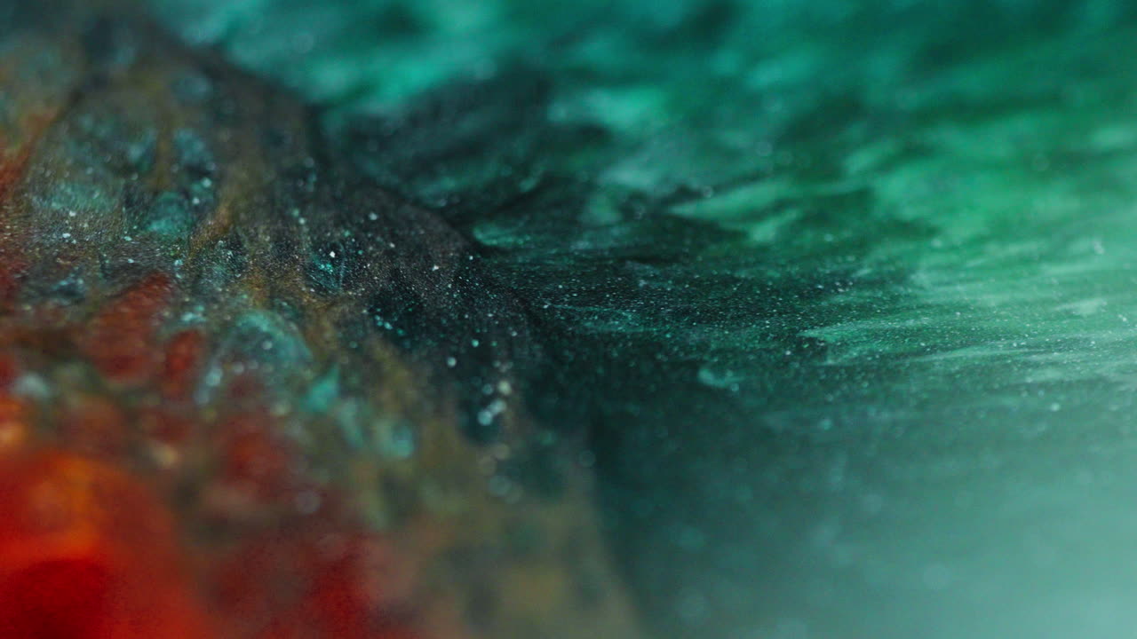 Macro view of green and orange glittery inks forming bubbles and wave-like patterns, resembling a snake skin texture