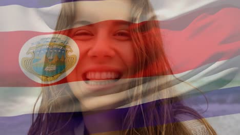 Animation-of-flag-of-costa-rica-waving-over-close-up-of-smiling-biracial-woman-standing-against-sea