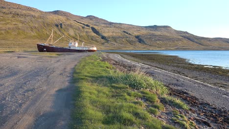 an abandoned fishing boat sits on the shore of the westfjords iceland