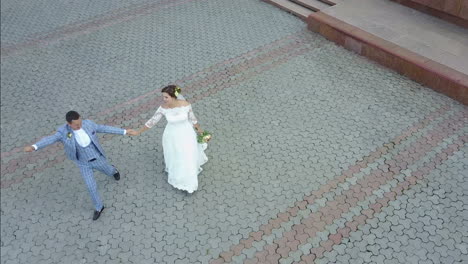 charming stylish newlyweds are holding hands while walking along the sunny town street. aerial view.