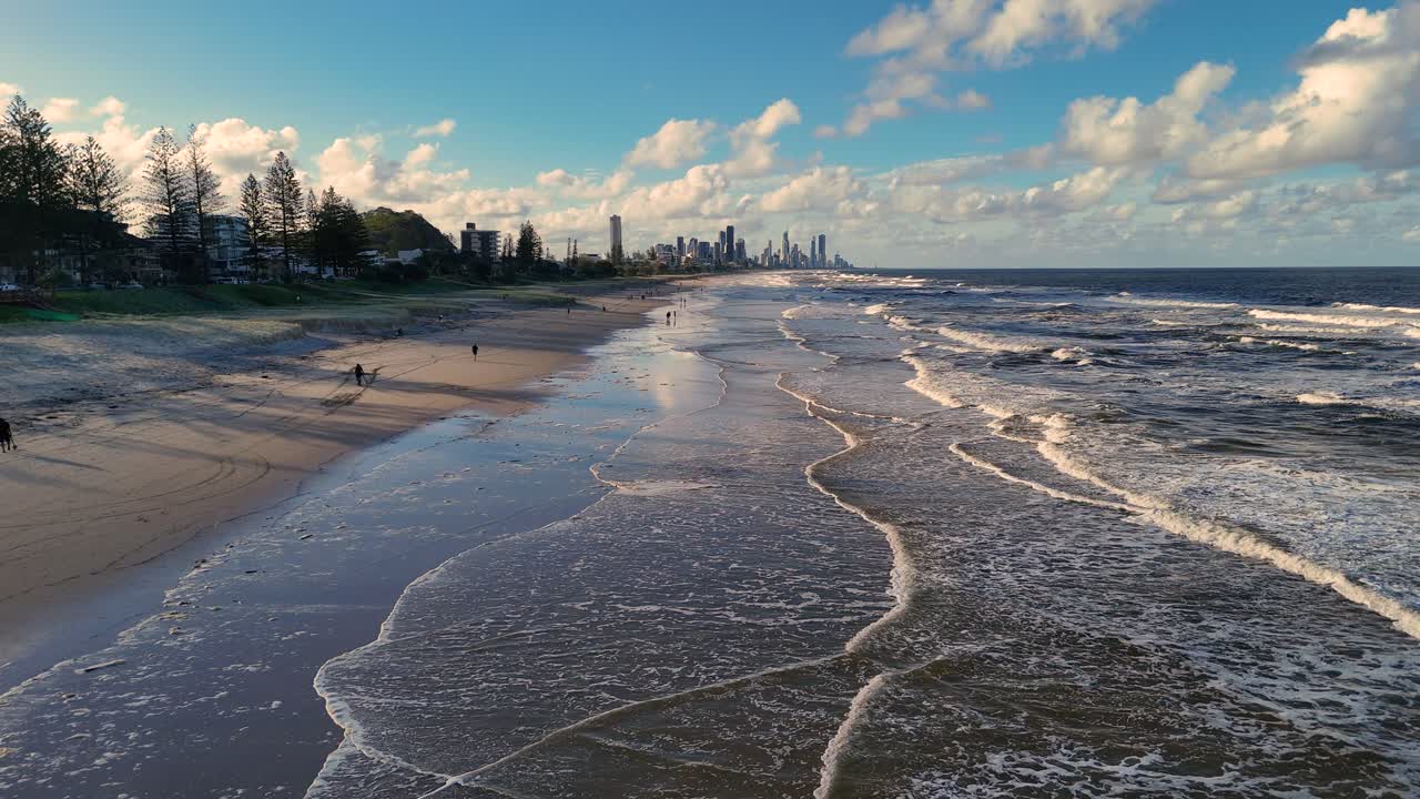 Aerial footage captures waves gently washing over a sandy beach at Gold Coast, Australia, under a bright, blue sky