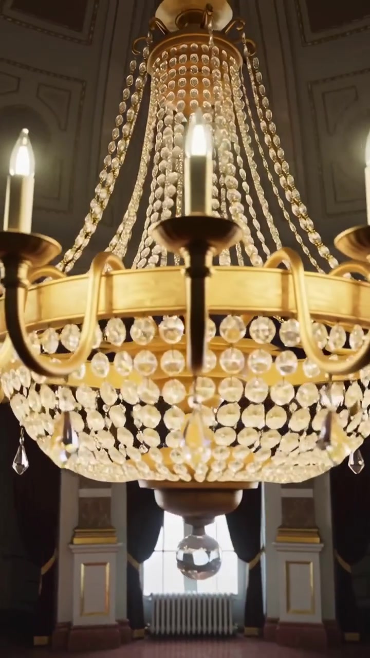 Video verticale: La telecamera si allontana, rivelando un lampadario d'oro in una grande sala per mostrare la brillantezza dei cristalli.