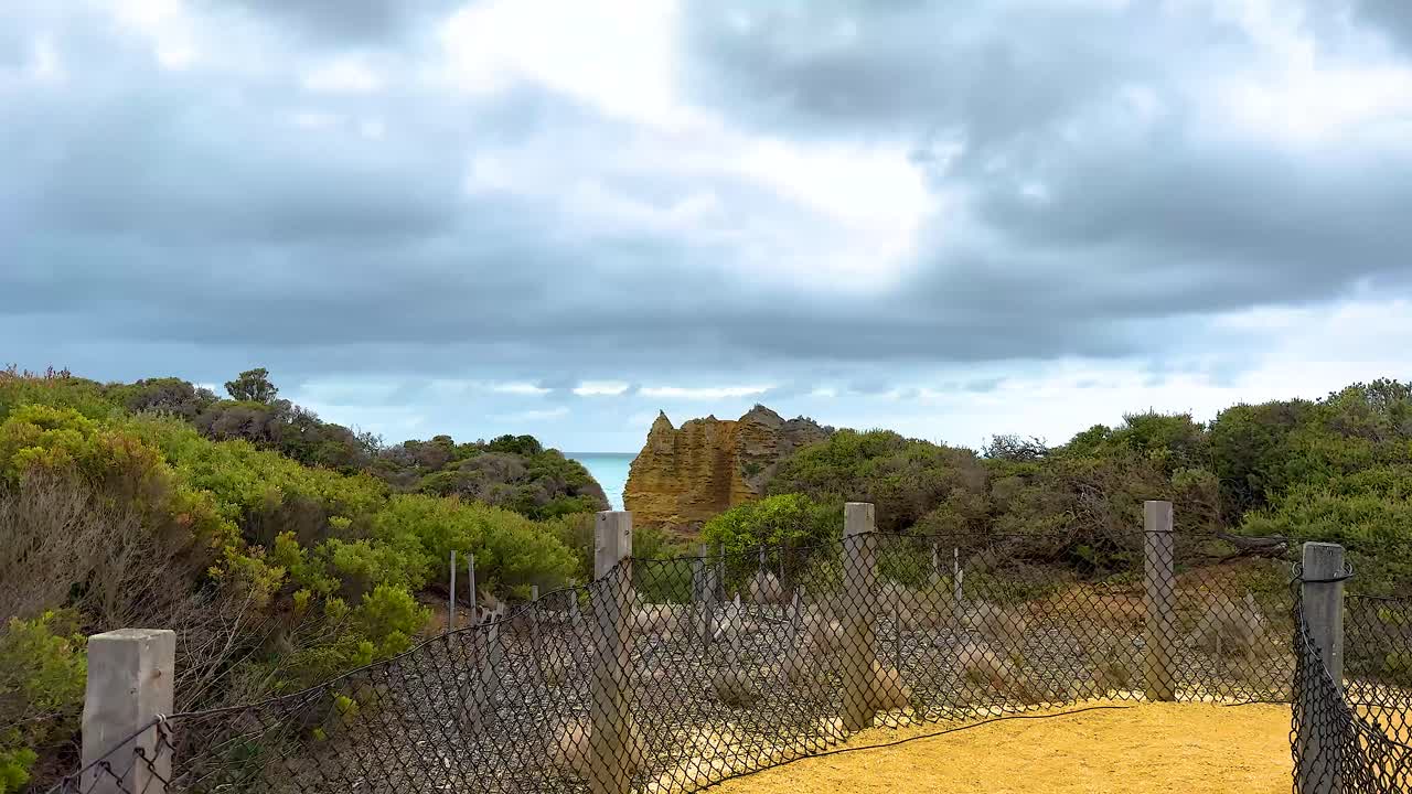 A serene coastal pathway with lush vegetation and distant cliffs under a cloudy sky, captured on Great Ocean Road