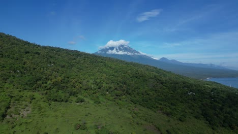 Clouds-cover-the-peak-of-Mount-Agung-volcano-in-Bali,-Indonesia-with-lush-green-fields-in-the-foreground,-aerial