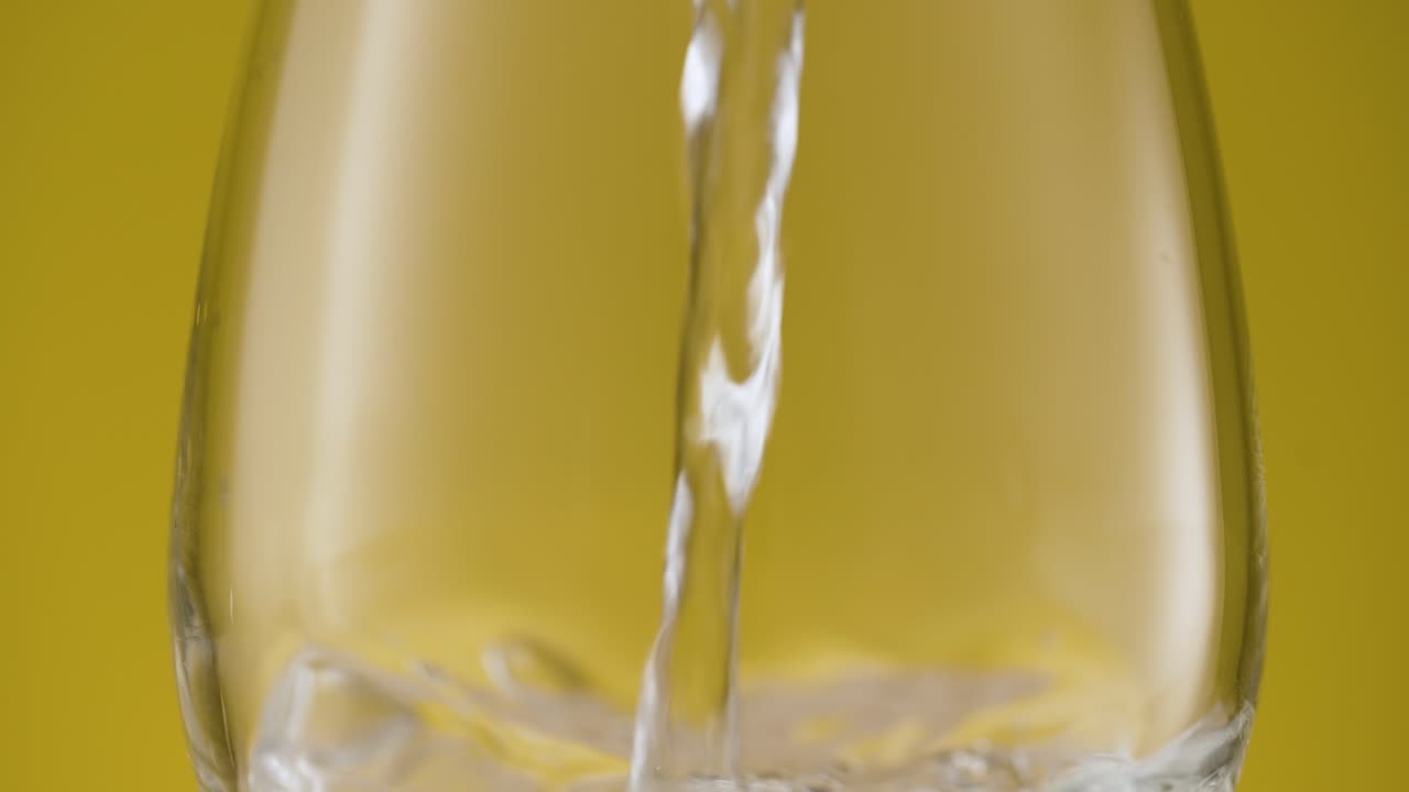 Filling a glass with fresh clean still water, isolated yellow background
