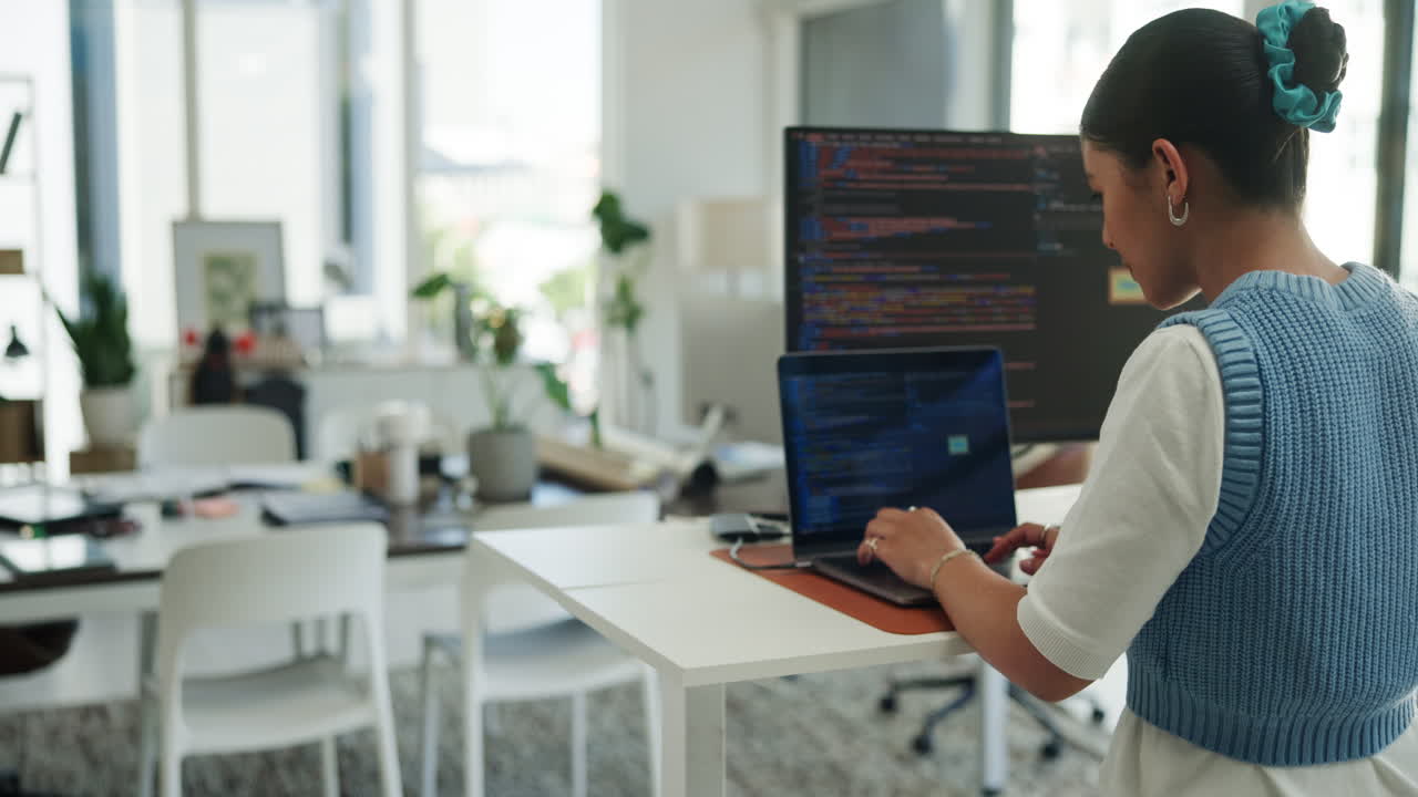 Young Woman Coding on Laptop at Standing Desk in Modern Office