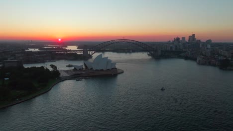 Royal-Botanic-Gardens-Sydney-Opera-House-Harbour-Bridge-Vivid-Australia-aerial-drone-tourist-city-Circular-Quay-scenic-helicopter-flight-ferry-boats-orange-dusk-evening-sunset-backwards-movement