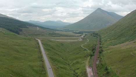 Stationary-aerial-shot-of-cars-driving-through-the-Scottish-highlands