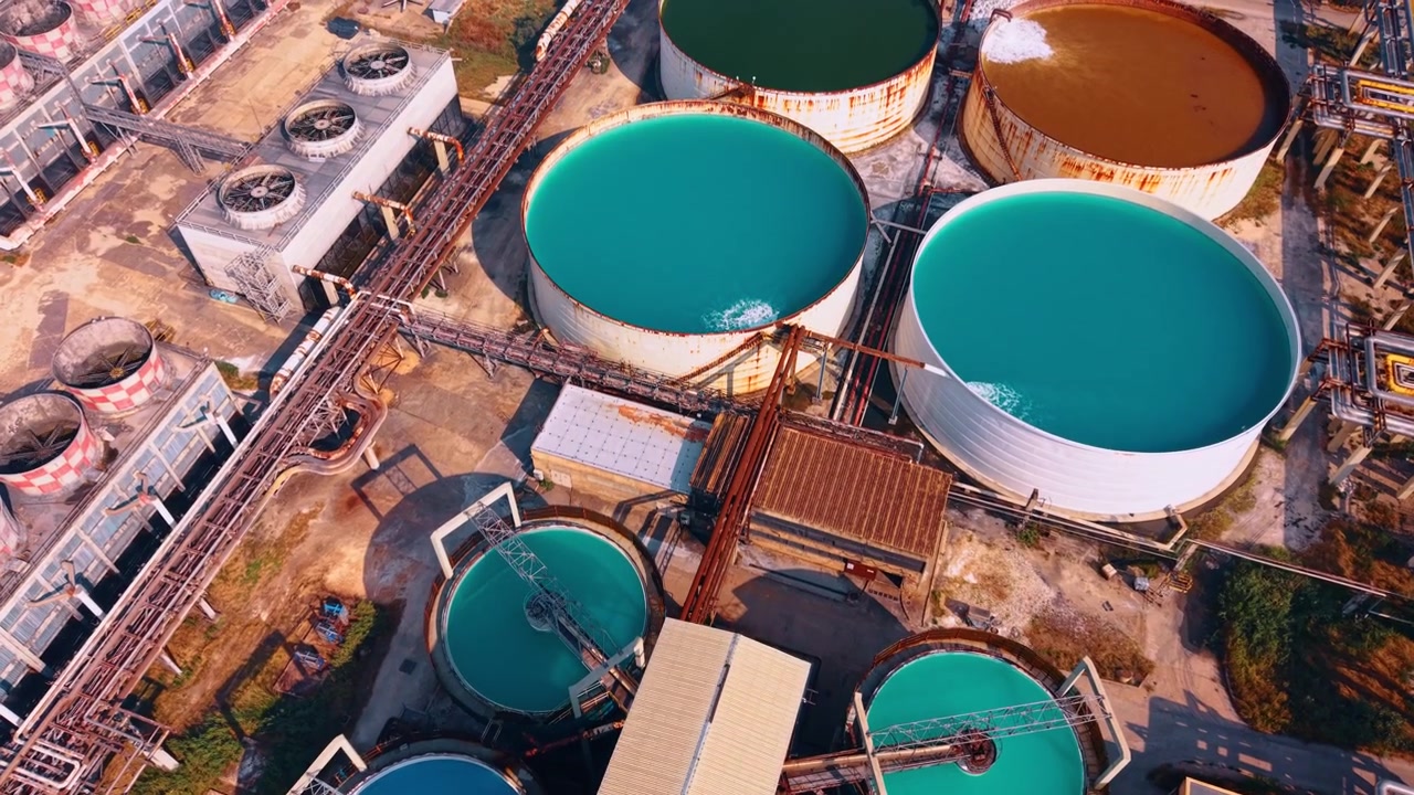 High angle shot of circular chemical treatment pools. Bright turquoise liquid fills round reservoirs connected by elevated pipe tracks at an industrial facility.